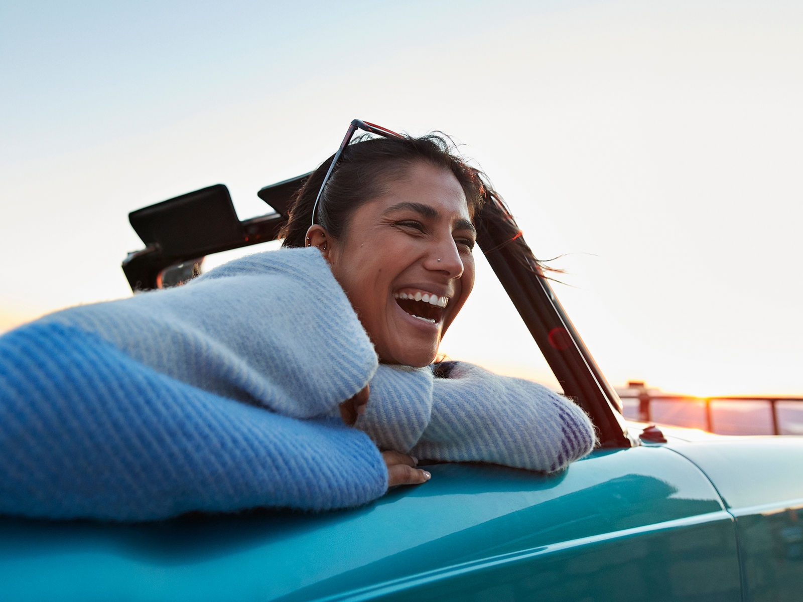 Cheerful young woman in convertible car enjoying road trip during sunset