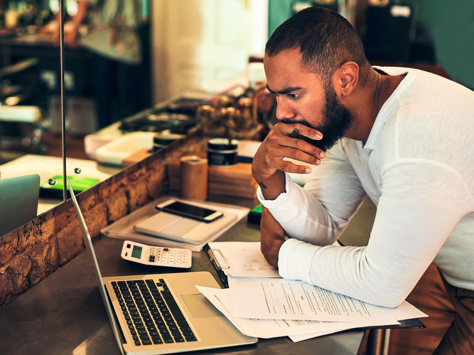 Un homme dans un salon de coiffure, debout devant un bureau avec un ordinateur portable et une calculatrice.