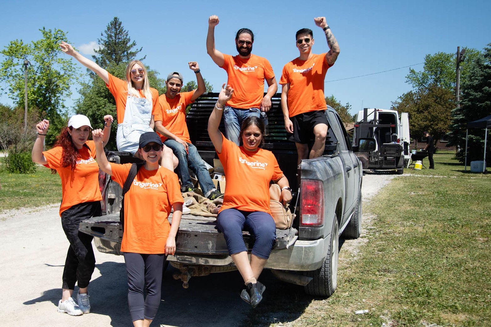 A group of Tangerine employees with their hands up in the air behind a pickup truck.