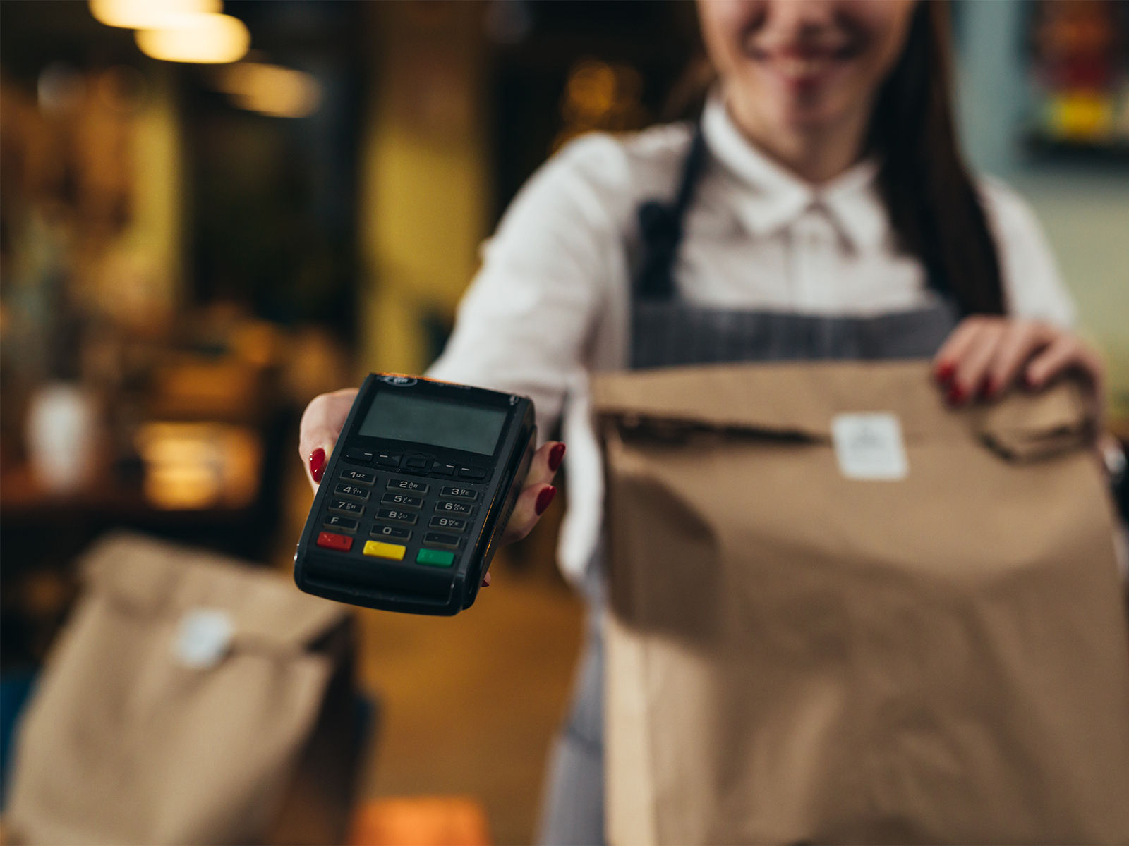 A smiling food service worker holding a card payment terminal towards a customer.