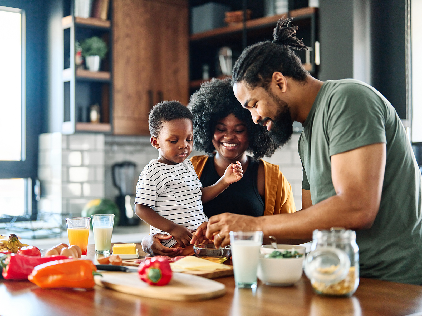 Un père, une mère et un jeune enfant dans une cuisine, préparant ensemble à manger.