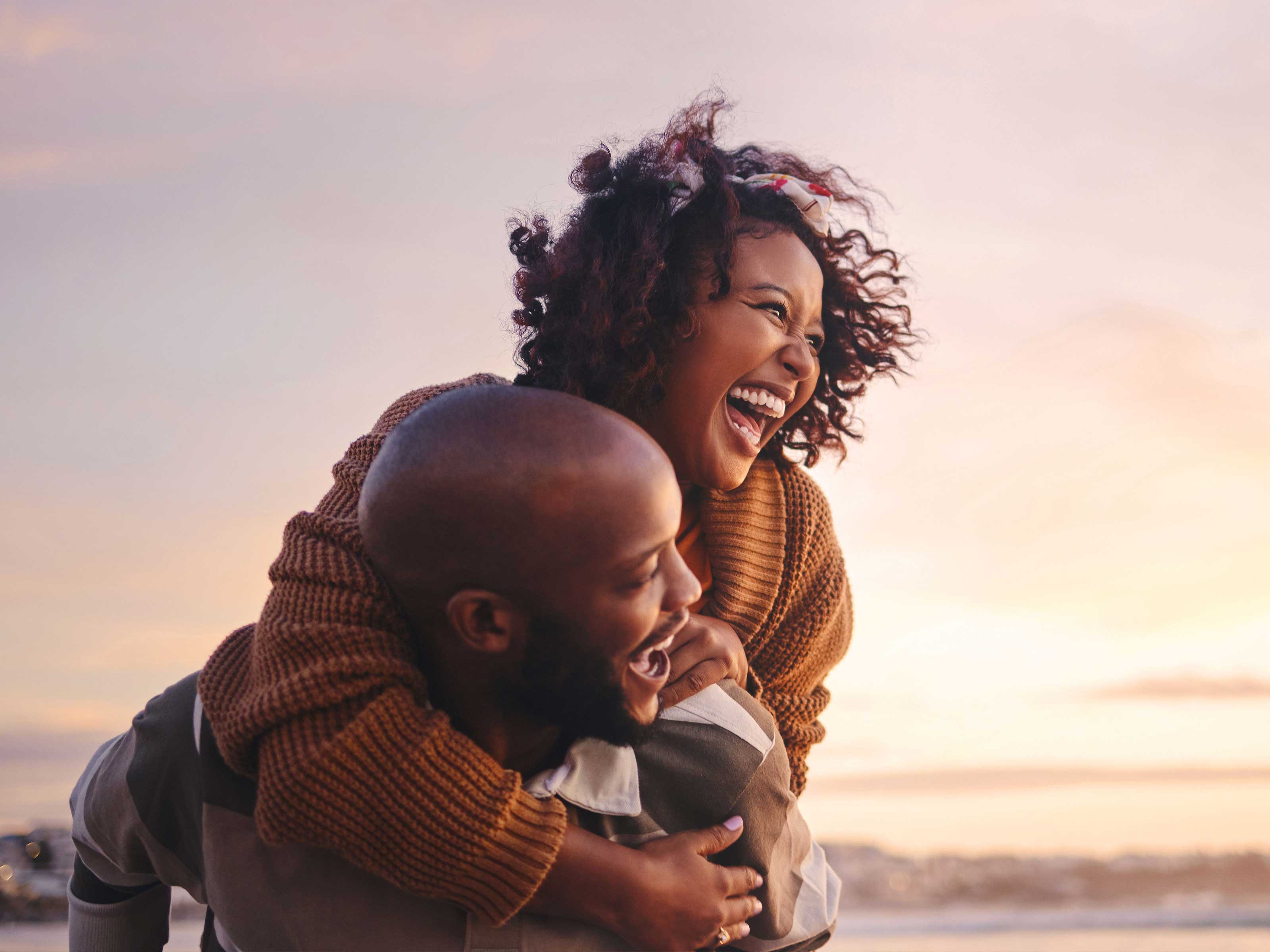 A smiling couple embrace at a beach as the sun sets.