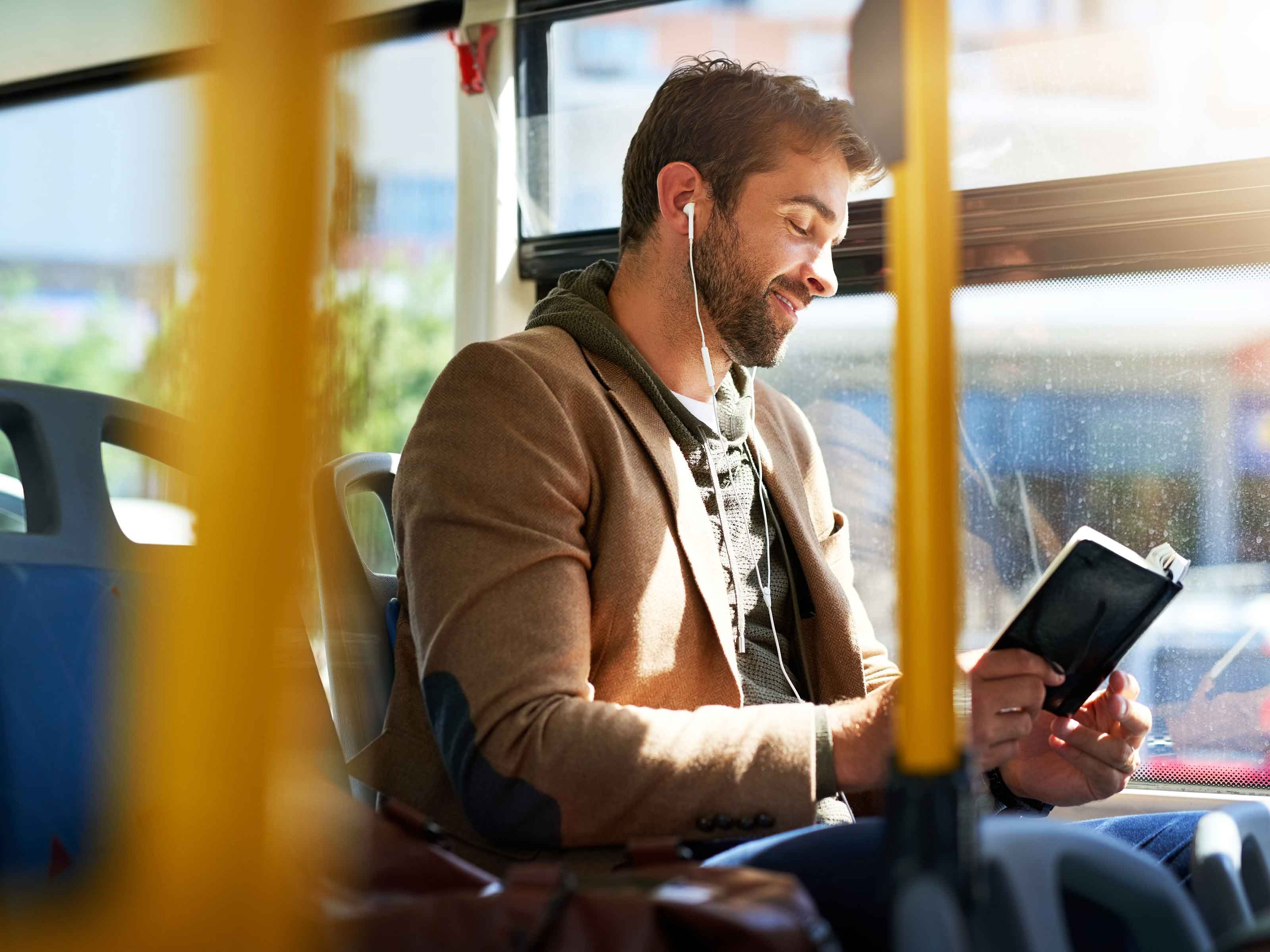 Un homme assis près de la fenêtre d'un bus, en train de lire un livre.