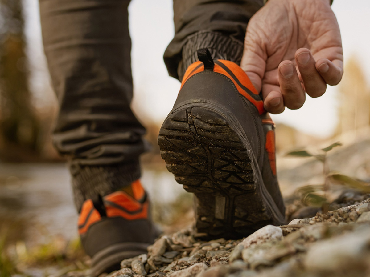 Close-up of a man's hand adjusting his hiking shoe on rocky terrain.